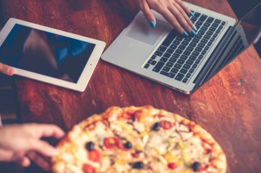 Masaüstü karışımı ofis aletleri, malzemeler ve ahşap ofis masasında pizza. Yukarıdan görüntüle.