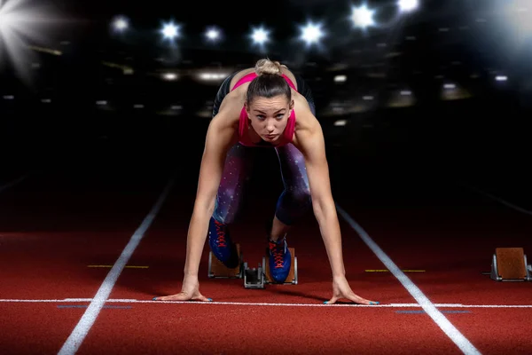 Woman sprinter leaving starting blocks on the athletic track. exploding start on stadium with reflectors — Stock Photo, Image