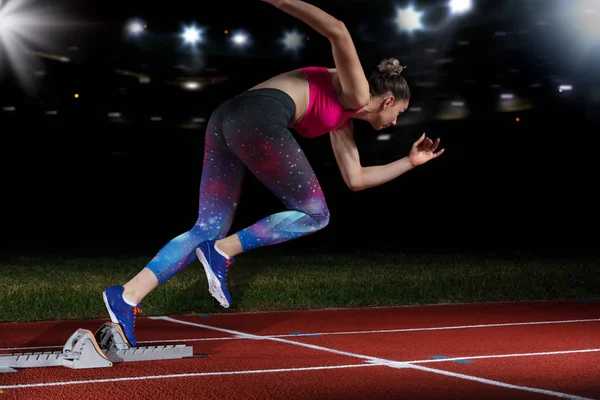 Mujer velocista dejando bloques de salida en la pista de atletismo. explosión de inicio en el estadio con reflectores — Foto de Stock