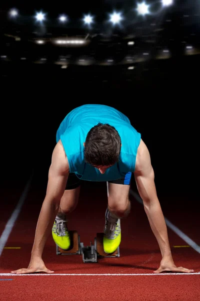 Sprinter laissant des blocs de départ sur la piste de course en face du grand stade moderne avec des lumières. Démarrage explosif . — Photo