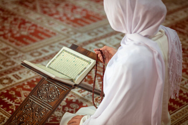 Молодая мусульманка молится в мечети с кураном

