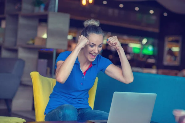 Chica ganadora eufórica viendo un portátil en una cafetería con una camisa azul —  Fotos de Stock