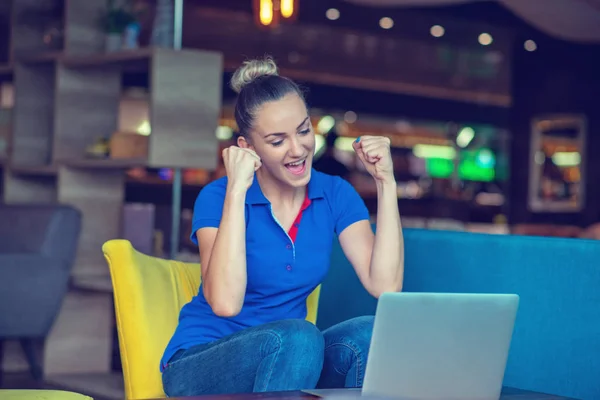 Chica ganadora eufórica viendo un portátil en una cafetería con una camisa azul —  Fotos de Stock