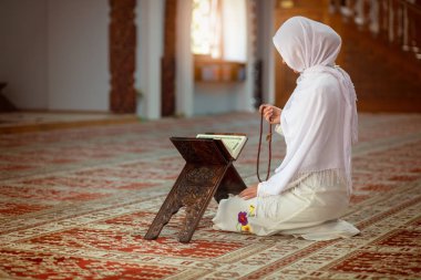 Young muslim woman praying in mosque with quran clipart