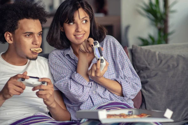 Imagem de jovem casal amoroso na cozinha em casa dentro de casa. Comer pizza e jogar jogos com console . — Fotografia de Stock