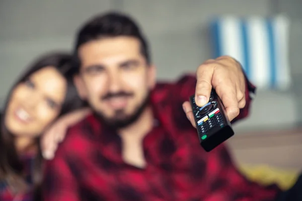 Couple fighting for remote control while watching TV at home