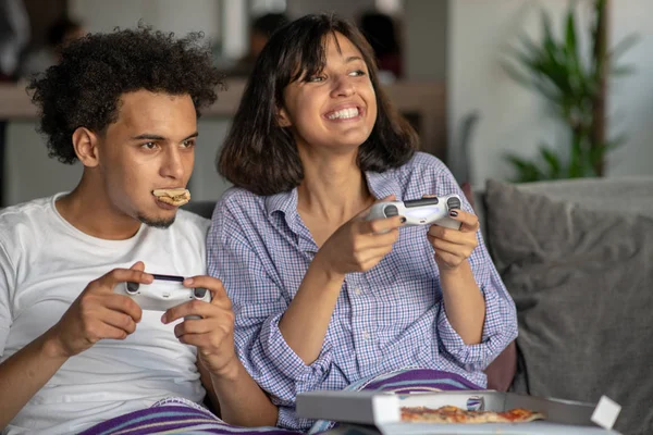 Imagen de pareja joven y cariñosa en la cocina en casa en interiores. Comer pizza y jugar con la consola . — Foto de Stock