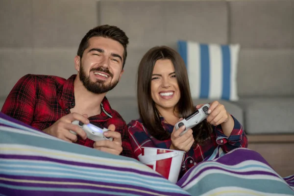 Casal apaixonado desfrutando de seu tempo livre, sentado em um sofá ao lado da janela, jogando videogames e se divertindo . — Fotografia de Stock