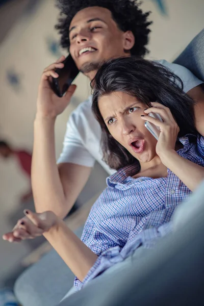 Atractiva pareja sentada en el sofá juntos mirando el teléfono inteligente en casa en la sala de estar — Foto de Stock