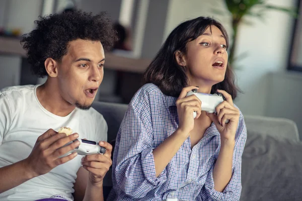 Image of young loving couple in kitchen at home indoors. Eating pizza and playing games with console.