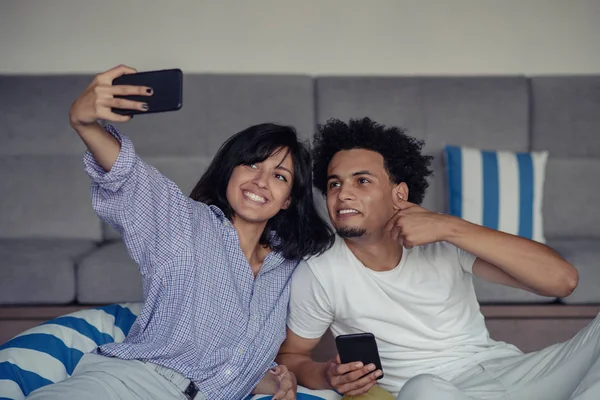 Sorrindo jovem casal tomando selfies na cama usando um smartphone, eles estão deitados e posando — Fotografia de Stock