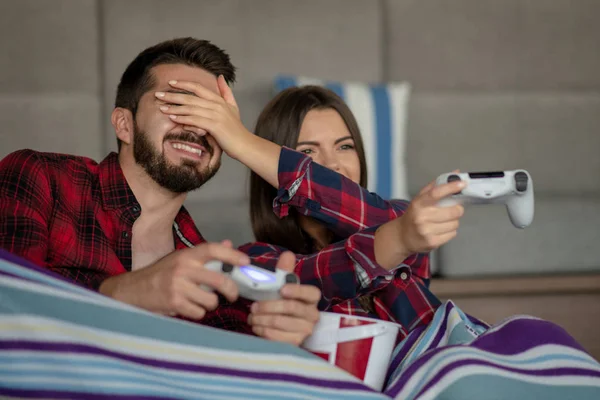 Pareja enamorada disfrutando de su tiempo libre, sentada en un sofá junto a la ventana, jugando videojuegos y divirtiéndose . — Foto de Stock