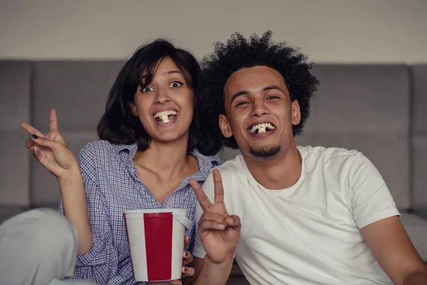 Bilden av leende par sitta på golvet nära soffa hemma och tittar åt sidan medan äta popcorn — Stockfoto