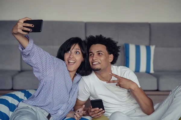 Sonriendo joven pareja tomando selfies en la cama usando un teléfono inteligente, están acostados y posando — Foto de Stock