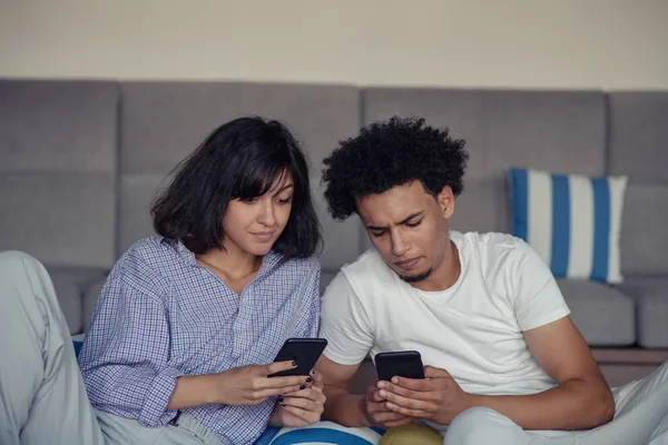 Casal relaxado ou amigos usando um telefone celular genérico juntos sentados em um sofá na sala de estar em casa — Fotografia de Stock