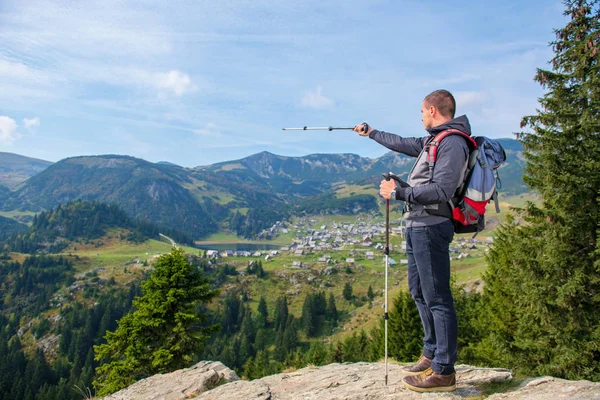 Caminhante jovem com mochila e postes de trekking em pé na borda do penhasco e olhando para o lago, visão traseira — Fotografia de Stock
