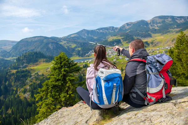 Dos excursionistas en el mirador en las montañas disfrutando de una hermosa vista del valle con un lago . — Foto de Stock