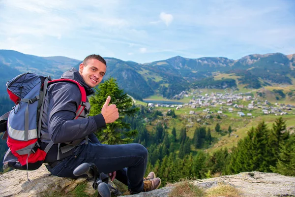 Joven excursionista masculino con mochila relajándose en la cima de una montaña durante el tranquilo día de verano . — Foto de Stock