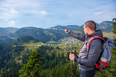 Uzun yürüyüşe çıkan kimse genç adam uçurumun kenarında duran ve gölde dikiz seyir sırt çantası ve trekking Polonyalılar ile