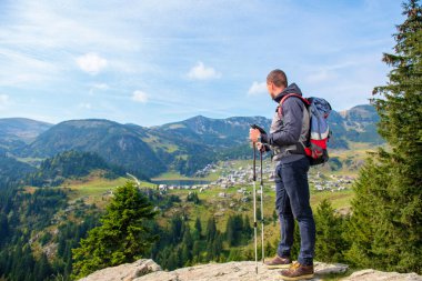 Uzun yürüyüşe çıkan kimse genç adam uçurumun kenarında duran ve gölde dikiz seyir sırt çantası ve trekking Polonyalılar ile