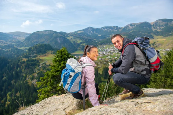 Två vandrare på viewpoint i bergen njuter av vacker utsikt över dalen med en sjö. — Stockfoto