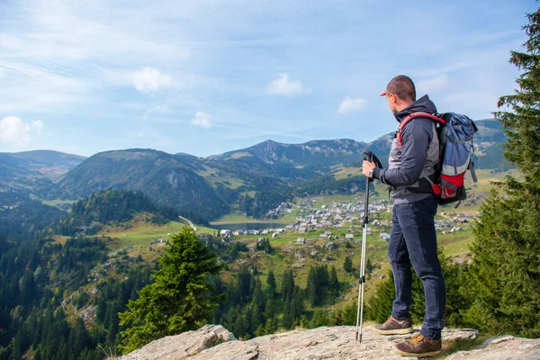 Tramp mladý muž s batoh a Treking hole stojící na okraji útesu a při pohledu na jezero, pohled zezadu — Stock fotografie