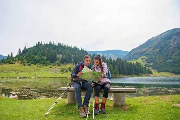 Vandring par. Unga par med ryggsäckar tittar på kartan intill sjö — Stockfoto