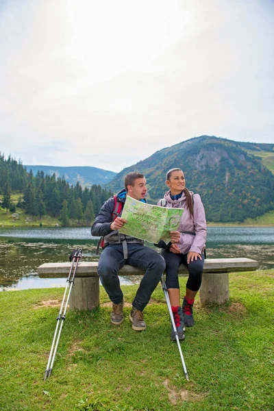Çift hiking. Göl yanında harita bakarak sırt çantaları ile genç Çift — Stok fotoğraf