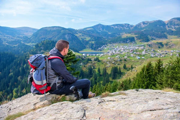 Mladý muž tramp s batohem relaxační na vrcholu hory v klidné letní den. — Stock fotografie