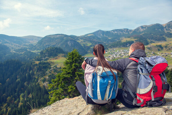 Two hikers at viewpoint in the mountains enjoying beautiful view of the valley with a lake.