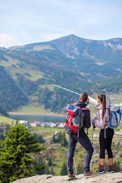 Couple of hikers showing the way with trekking poles up on the mountain peak — Stock Photo, Image