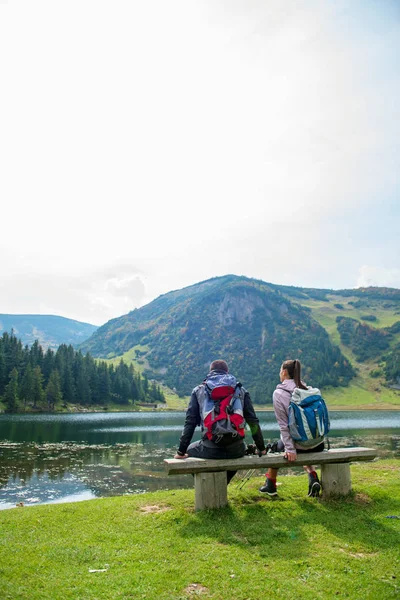 Mladý pár batůžkářů blízko jezera v horách — Stock fotografie