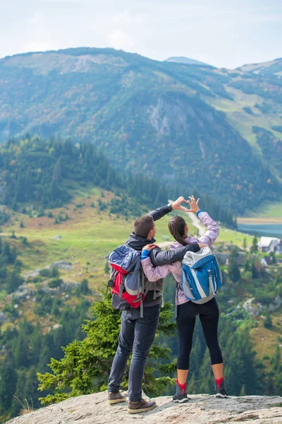 Två vandrare på viewpoint i bergen njuter av vacker utsikt över dalen med en sjö. — Stockfoto