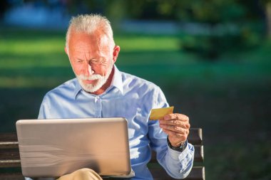 Eski erkek bankta oturan ve online kavramı alışveriş laptop Park, net sörf