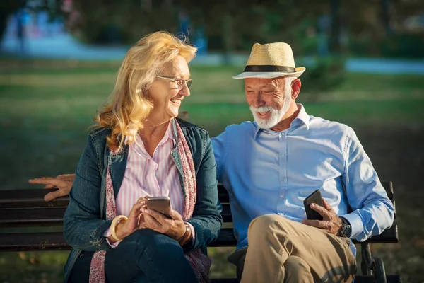 La vejez, la tecnología y el concepto de personas - feliz pareja de personas mayores con teléfonos inteligentes en el parque de verano —  Fotos de Stock