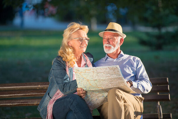 Портрет счастливого мужчины и женщины, читающих карту, сидя на скамейке в парке. Старшая пара на отдыхе с использованием карты города
.