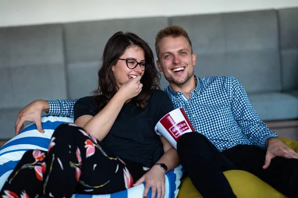 Porträt eines aufgeregten jungen Paares, das es sich zu Hause auf einer Couch gemütlich macht, während es fernsieht und Popcorn isst — Stockfoto