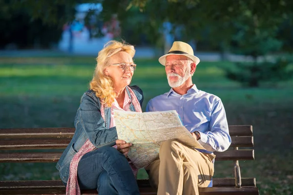 Retrato de homem feliz e mulher lendo mapa enquanto sentado em um banco de parque. Casal de idosos em férias usando o mapa da cidade . — Fotografia de Stock