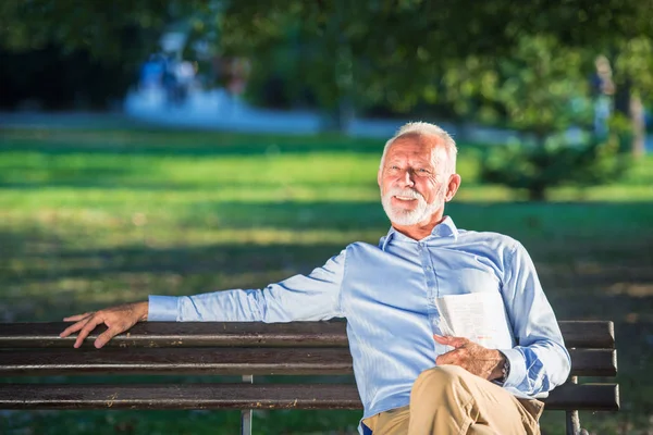 Hombre mayor relajándose en el parque en un día soleado sentado en un banco de madera y esperando a alguien — Foto de Stock