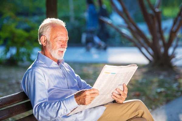 Retrato de um homem sênior lendo jornais no parque . — Fotografia de Stock