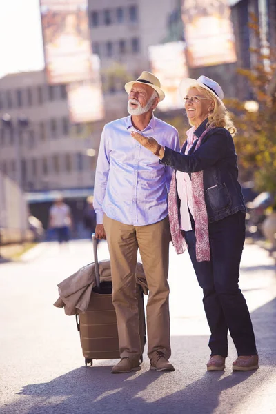 Feliz alegre pareja de turistas mayores con mapa y guía de la ciudad caminando por la calle —  Fotos de Stock