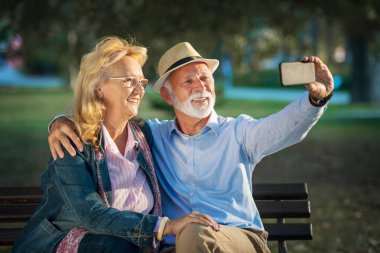 Yaşlı çift parkta akıllı telefonlarıyla selfie çekiyor.