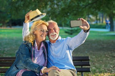Yaşlı çift parkta akıllı telefonlarıyla selfie çekiyor.