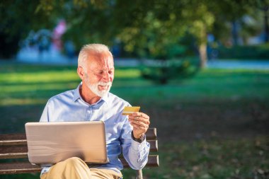 Eski erkek bankta oturan ve online kavramı alışveriş laptop Park, net sörf