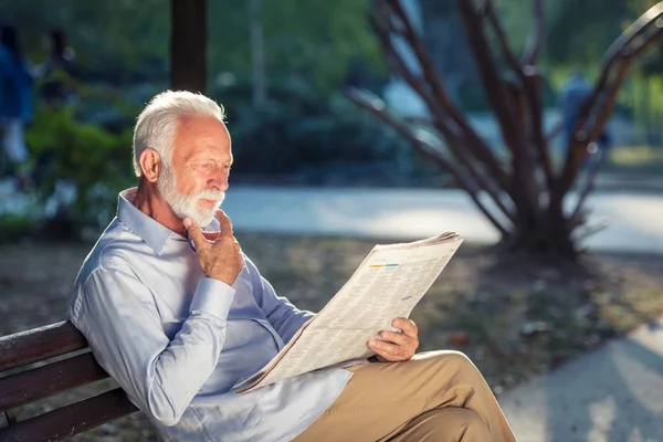 Retrato de un hombre mayor leyendo periódicos en el parque . — Foto de Stock