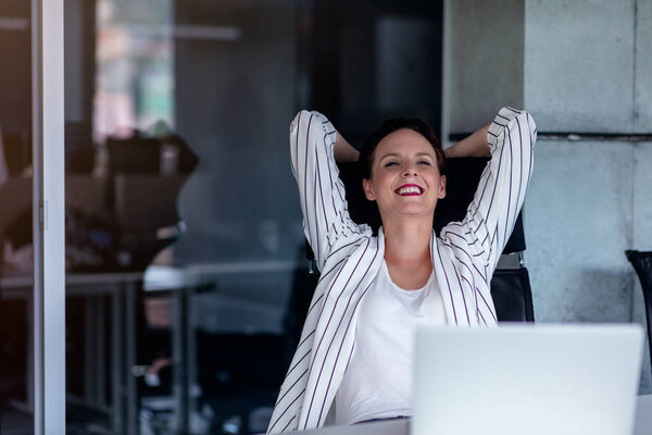 Relaxing at working place. Attractive young woman holding hands behind head and keeping eyes closed while sitting at her working place