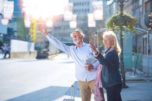 Asistir a una nueva ciudad. Longitud completa de optimista anciano y mujer están de pie cerca de la carretera y tratando de coger un taxi . —  Fotos de Stock