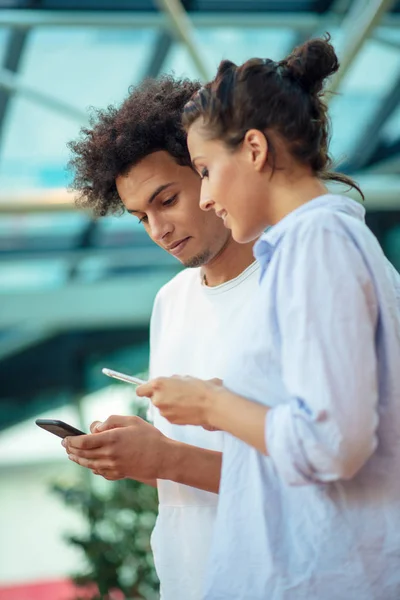 Digital technology and traveling. Young loving couple in casual wear using smartphone while standing in the airport terminal waiting for boarding. — Stock Photo, Image