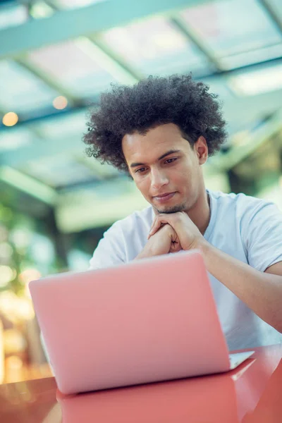 Serious Afro American mężczyzna student w T-shirt siedzi w kawiarni picie kawy na wynos pracy w jego projekt za pomocą laptopa — Zdjęcie stockowe