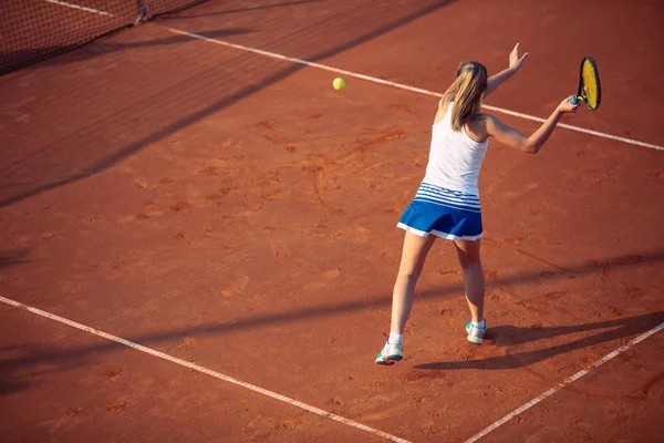 Young woman playing tennis on clay. Forehand.